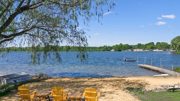 A lakeside setting with a sandy beach, wooden chairs, and a dock with a boat. - Large Updated Lakefront House on Lake George. Kayaks, games, fire pit, sledding. (West Branch)