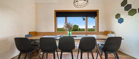 Un'area pranzo con un tavolo grande e sei sedie, una lampada a sospensione e vista sull'esterno attraverso un'ampia finestra.