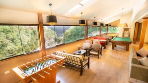 A spacious room with a foosball table, pool table, and comfortable seating. Large windows offer a view of the outdoors. - Santuario Machupicchu (Machu Picchu)