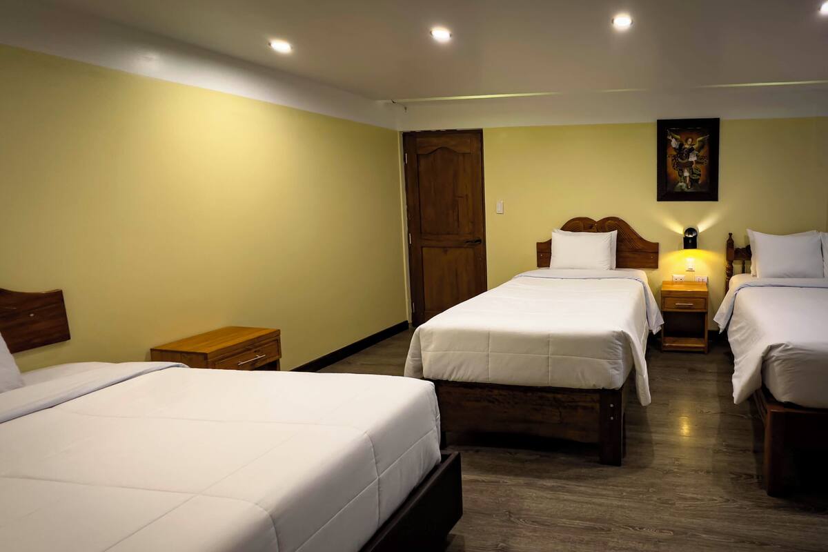 A hotel room with three single beds, wooden headboards, and a wooden floor.