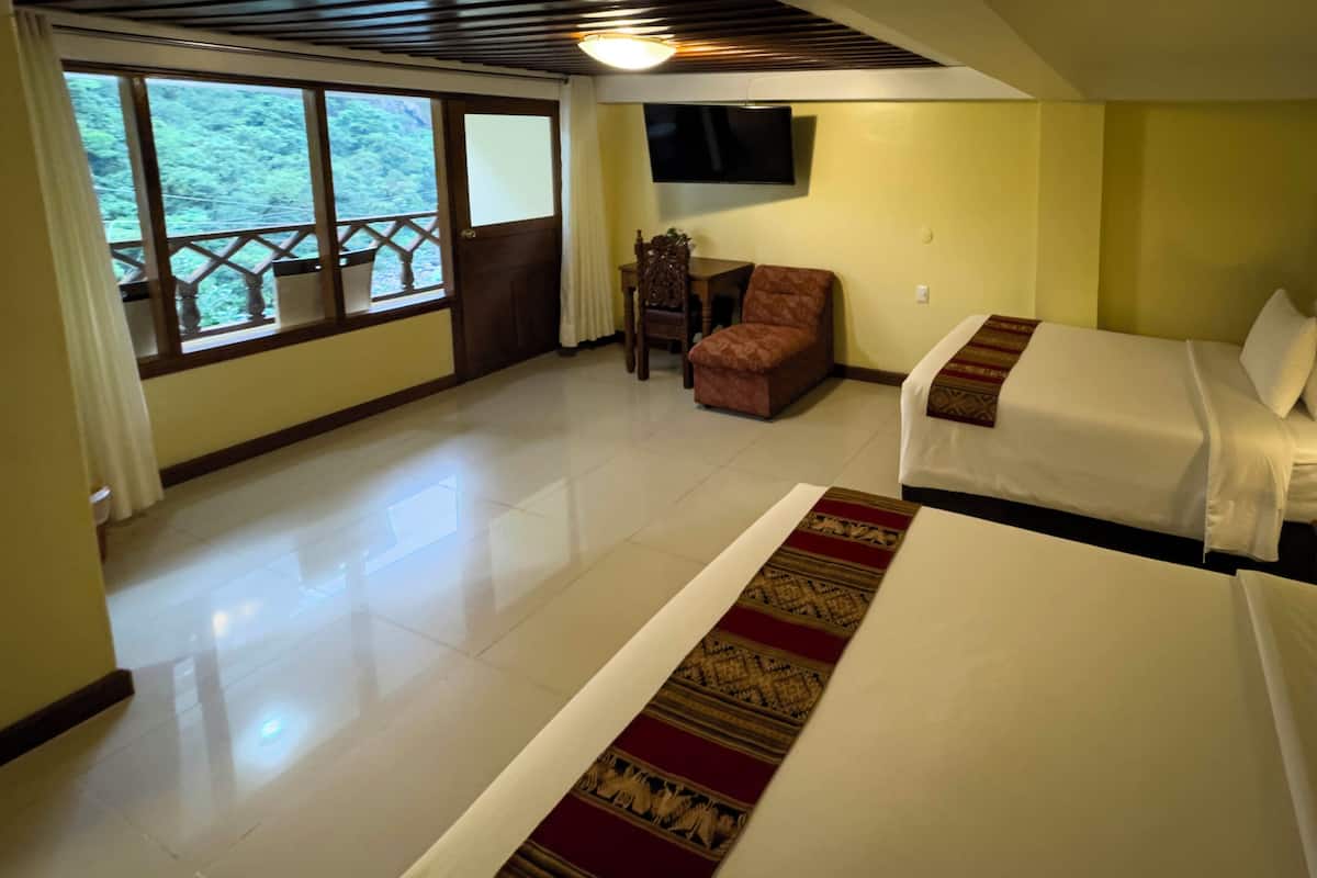 A hotel room with two beds, a wooden chair, a small table, a TV on the wall, and a balcony with a view of the forest.