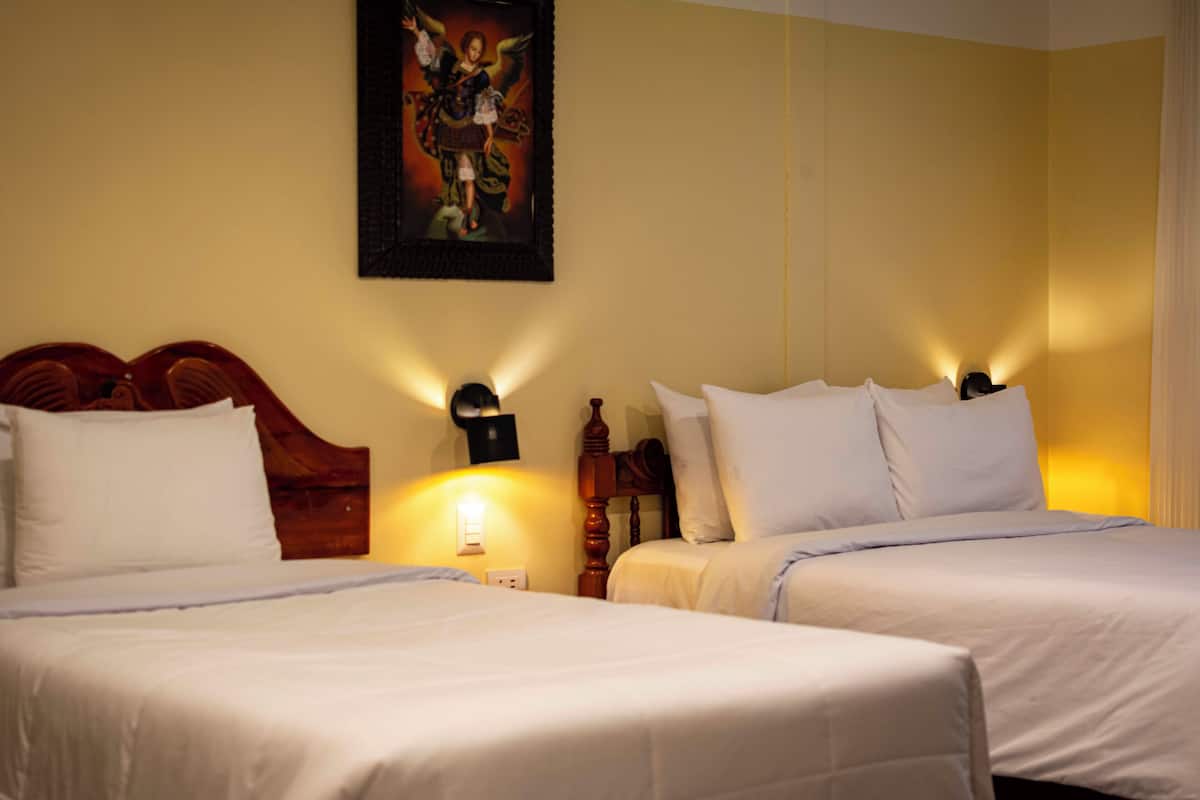 A hotel room with two beds, a wooden headboard, a wall-mounted lamp, and a framed picture.