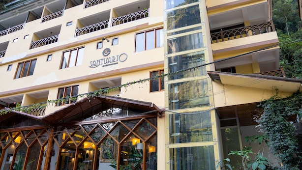 A multi-story hotel with a prominent glass elevator shaft, balconies, and a stone facade. - Santuario Machupicchu (Machu Picchu)