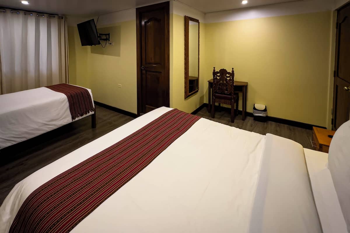 A hotel room with two single beds, a wooden chair, a small table, a mirror, and a television on the wall.