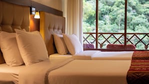 A hotel room with a large bed, a headboard, and a window with a view of trees. - Santuario Machupicchu (Machu Picchu)