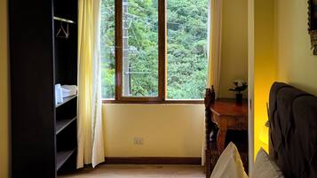 A room with a large window, a wardrobe, a desk, and a bed.