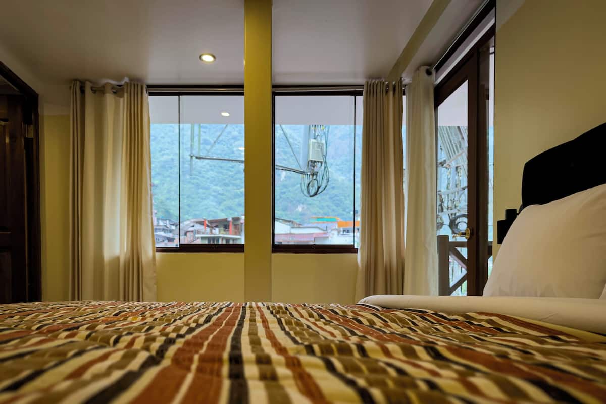 A hotel room with a large bed, a window with curtains, and a view of buildings outside.