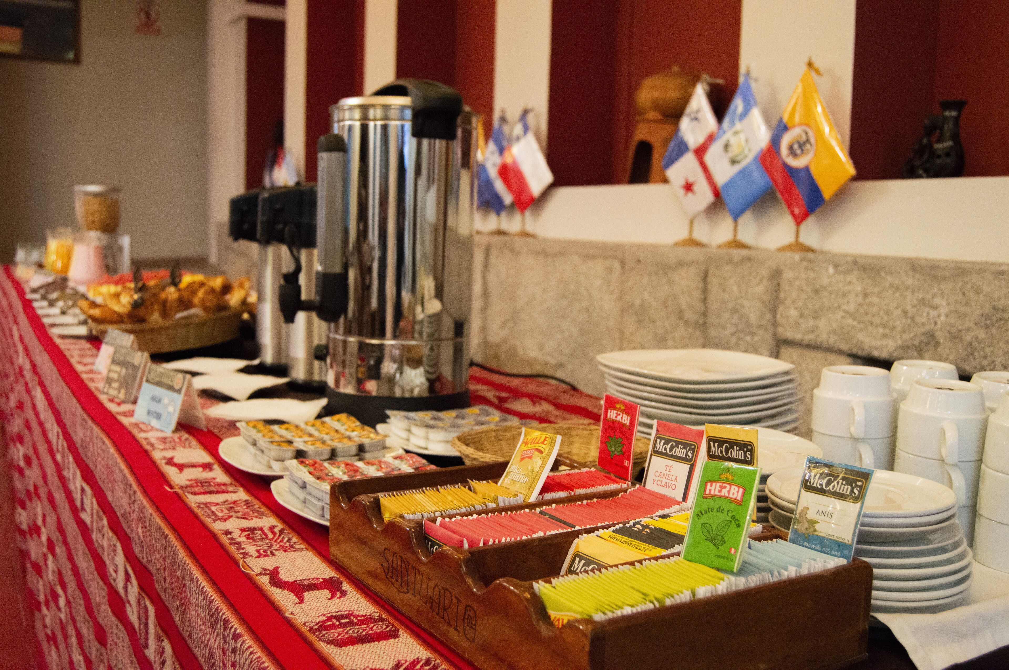 A buffet table with various food items, a coffee machine, and flags in the background.