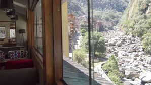 A room with a large window overlooking a mountainous area with a river and buildings. - Santuario Machupicchu (Machu Picchu)