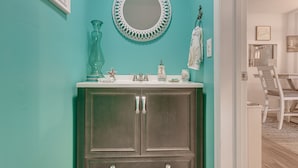 A bathroom with teal walls, a round mirror, a sink, and a cabinet. - Coastal St Simons Retreat Near Gascoigne Bluff! (St Simons Island)