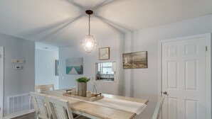 A dining area with a wooden table and chairs, a hanging light fixture, and a white door. - Coastal St Simons Retreat Near Gascoigne Bluff! (St Simons Island)