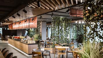 A modern restaurant interior with wooden tables and chairs, a central bar area, and vertical gardens.