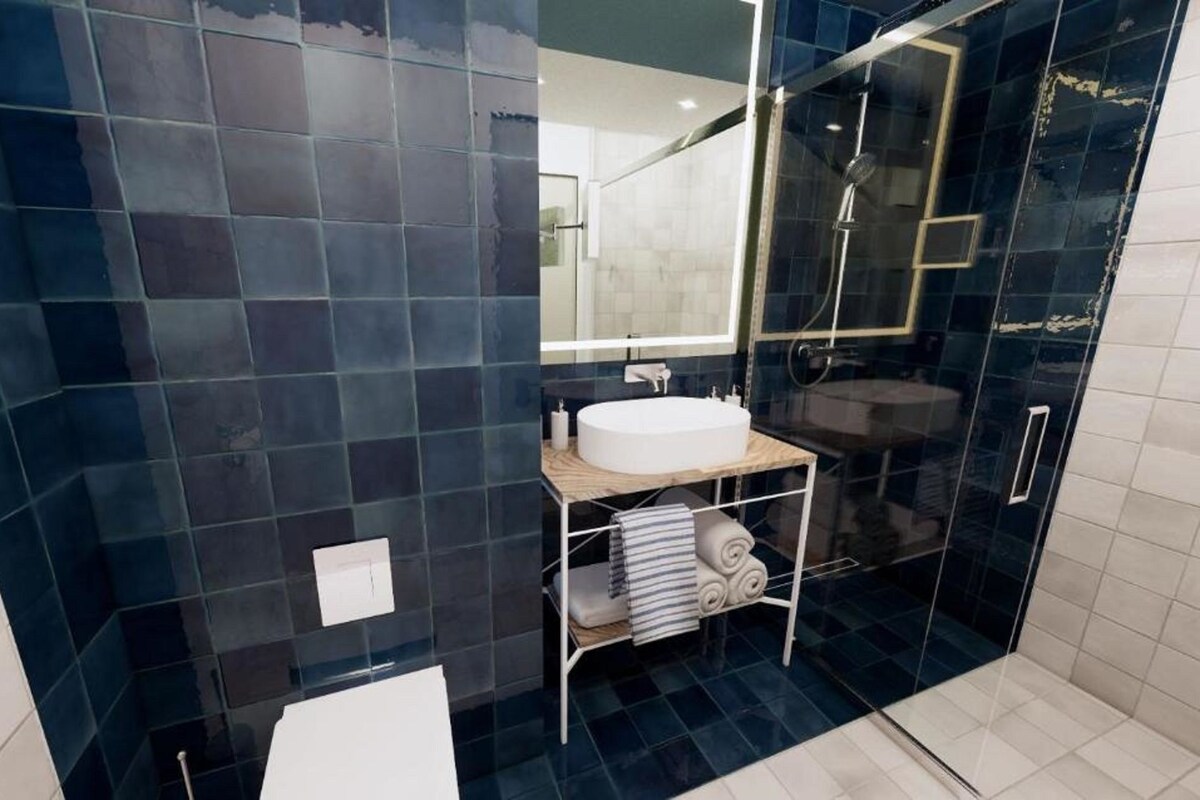 A modern bathroom with dark blue tiles, a white sink, a glass-enclosed shower, and a towel rack with towels.