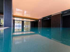 A modern indoor swimming pool with clear glass walls, a tiled floor, and a view of the outside. - Mercure Sibiu Arsenal (Sibiu)