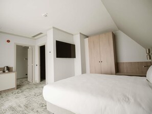 A modern bedroom with a large bed, a TV mounted on the wall, a wardrobe, and a desk with a kettle. - Mercure Sibiu Arsenal (Sibiu)