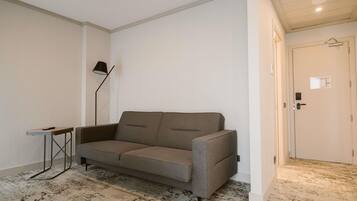 A neutral-colored room with a grey sofa, a small side table, a floor lamp, and a door with a hanging coat rack.