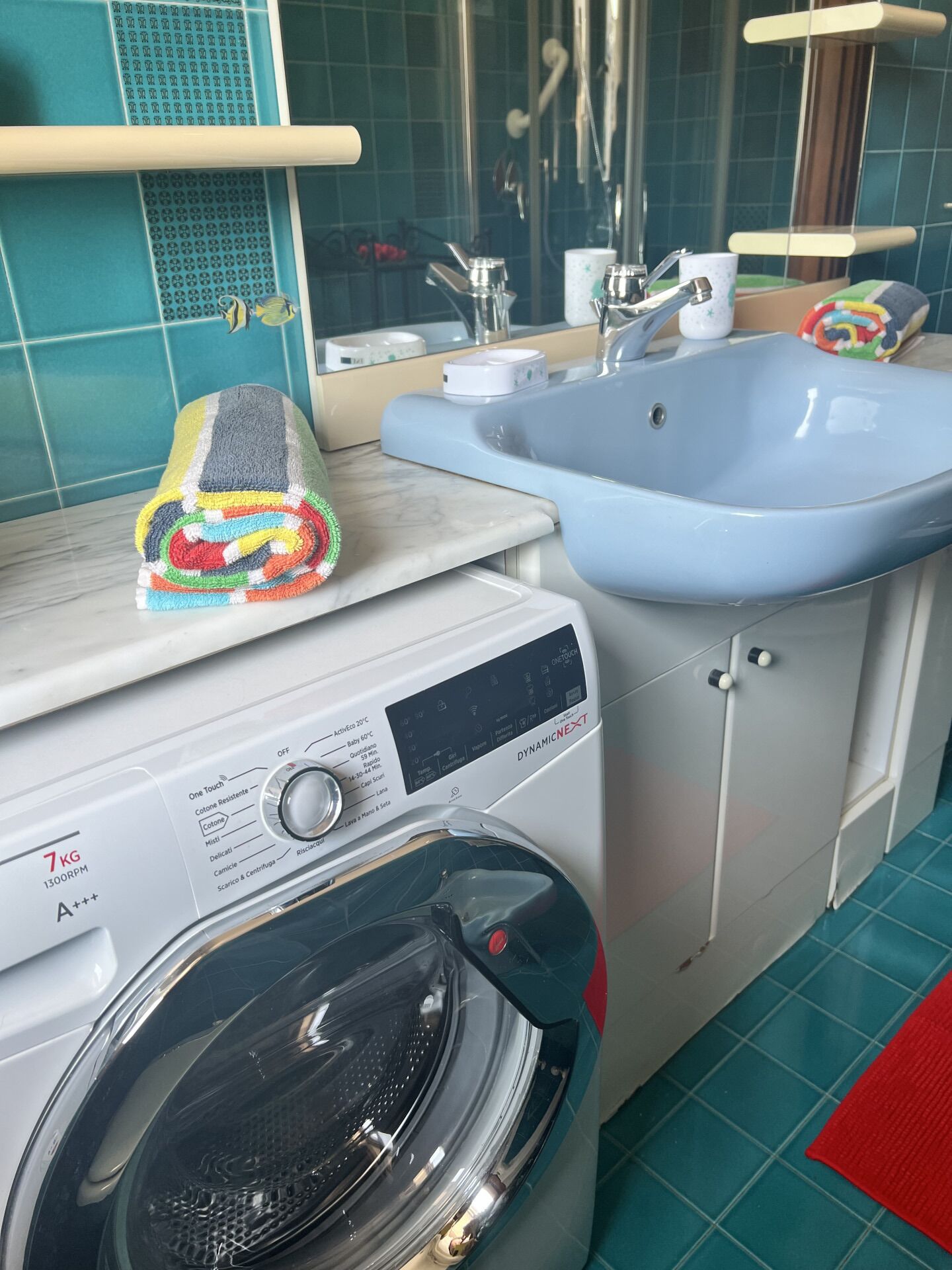 A compact laundry area with a front-loading washing machine, a sink, and a mirror.