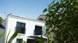 A white building with two windows and a balcony, surrounded by greenery. - Large refurbished house in central village location (Dompierre-sur-Mer)