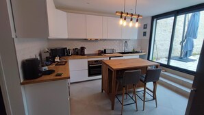 A modern kitchen with white cabinets, a wooden island, and a large window offering a view of the outdoors. - Large refurbished house in central village location (Dompierre-sur-Mer)