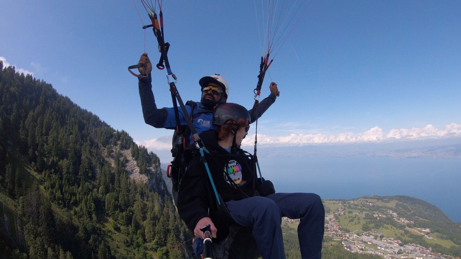 Eine Person tandemparagliding, mit Gurtschloss und Helm, mit Blick auf eine gebirgige Landschaft und ein Tal darunter.