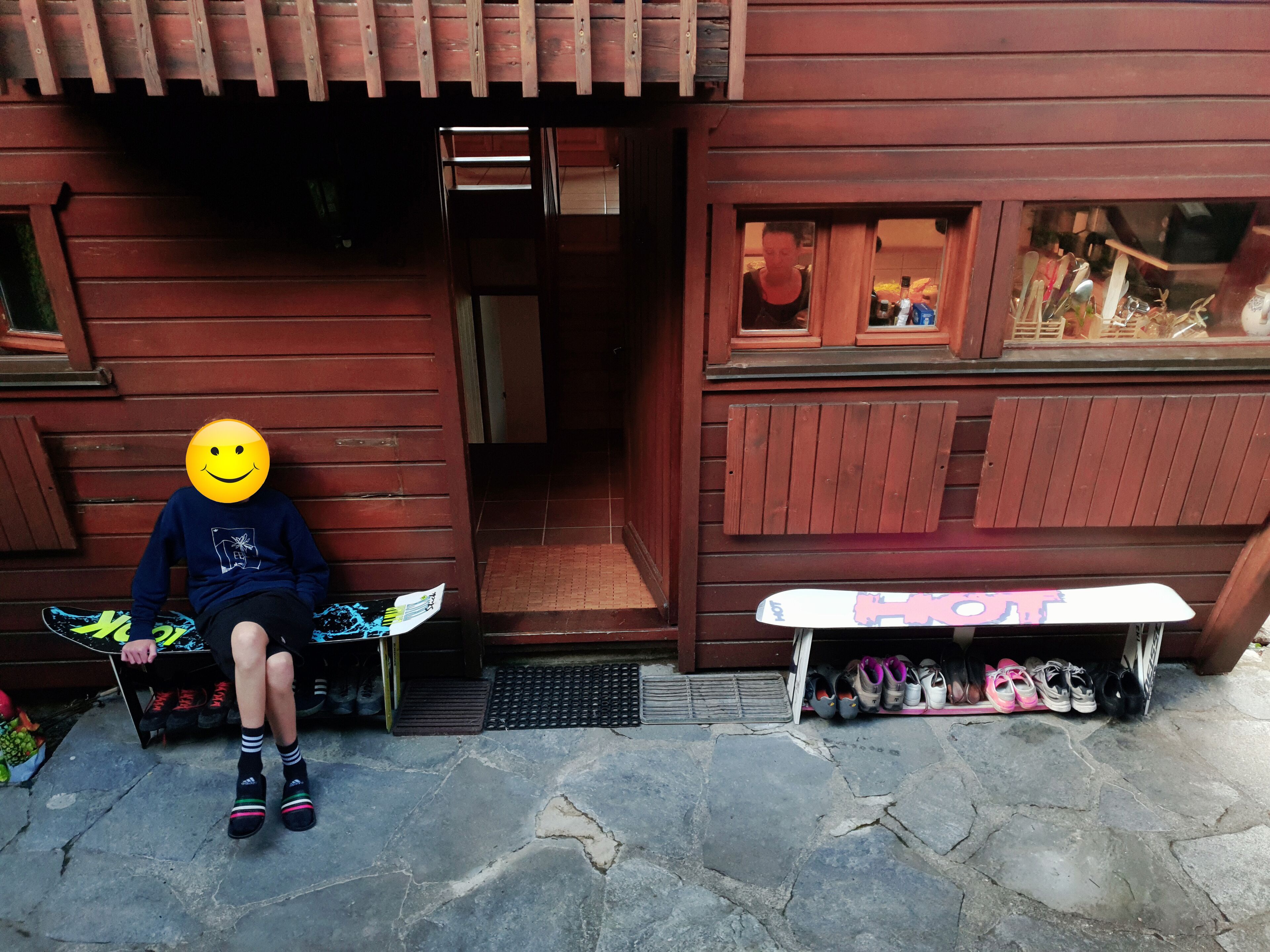 A person sitting on a chair outside a wooden building with a staircase leading inside.