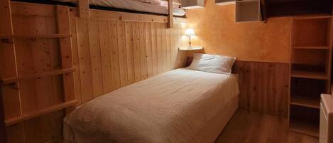A cozy, compact room with a bunk bed, a bedside table with a lamp, and built-in shelves with books and decorative items.