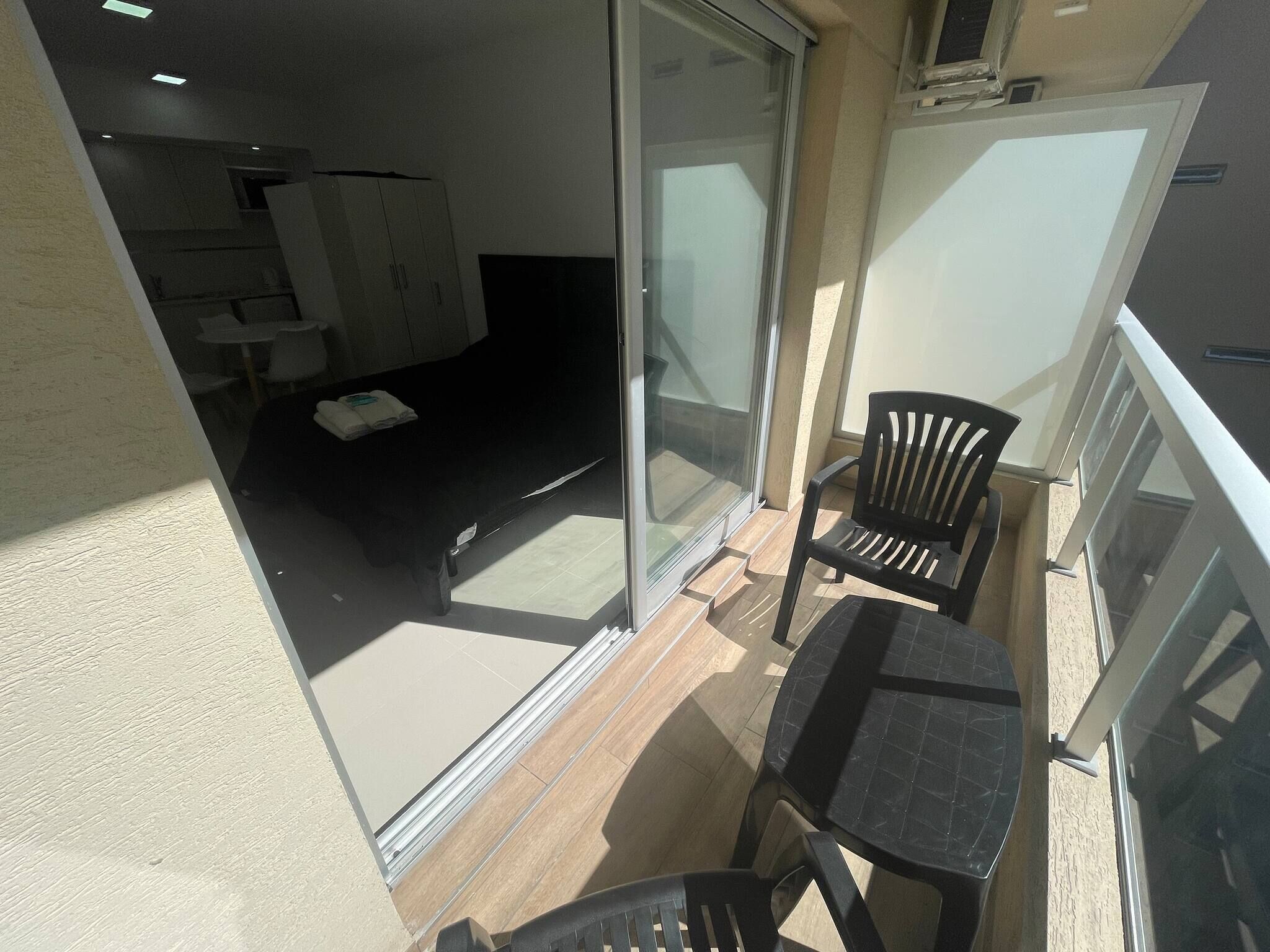 A balcony with a glass door leading to a room with a bed, a chair, and a table.