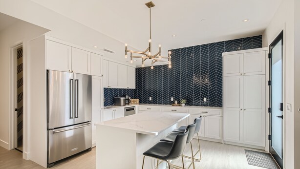 A modern kitchen with white cabinetry, a stainless steel refrigerator, a central island with bar stools, and a black and white herringbone backsplash. - Luxurious Rental with Ideal Downtown Proximity - Stroll to Pearl Street and CU. (Boulder)
