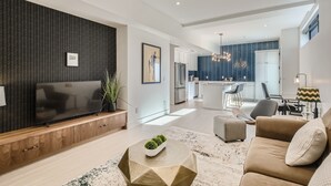 A modern living room with a flat-screen TV, a coffee table with a plant, and a sofa with a cushion. - Luxurious Rental with Ideal Downtown Proximity - Stroll to Pearl Street and CU. (Boulder)