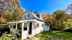 A single-story house with a porch, a small attached garage, and a well-maintained lawn. - Jewel Brook Cottage- 4BR house on a tranquil flowing brook!  (Ludlow)
