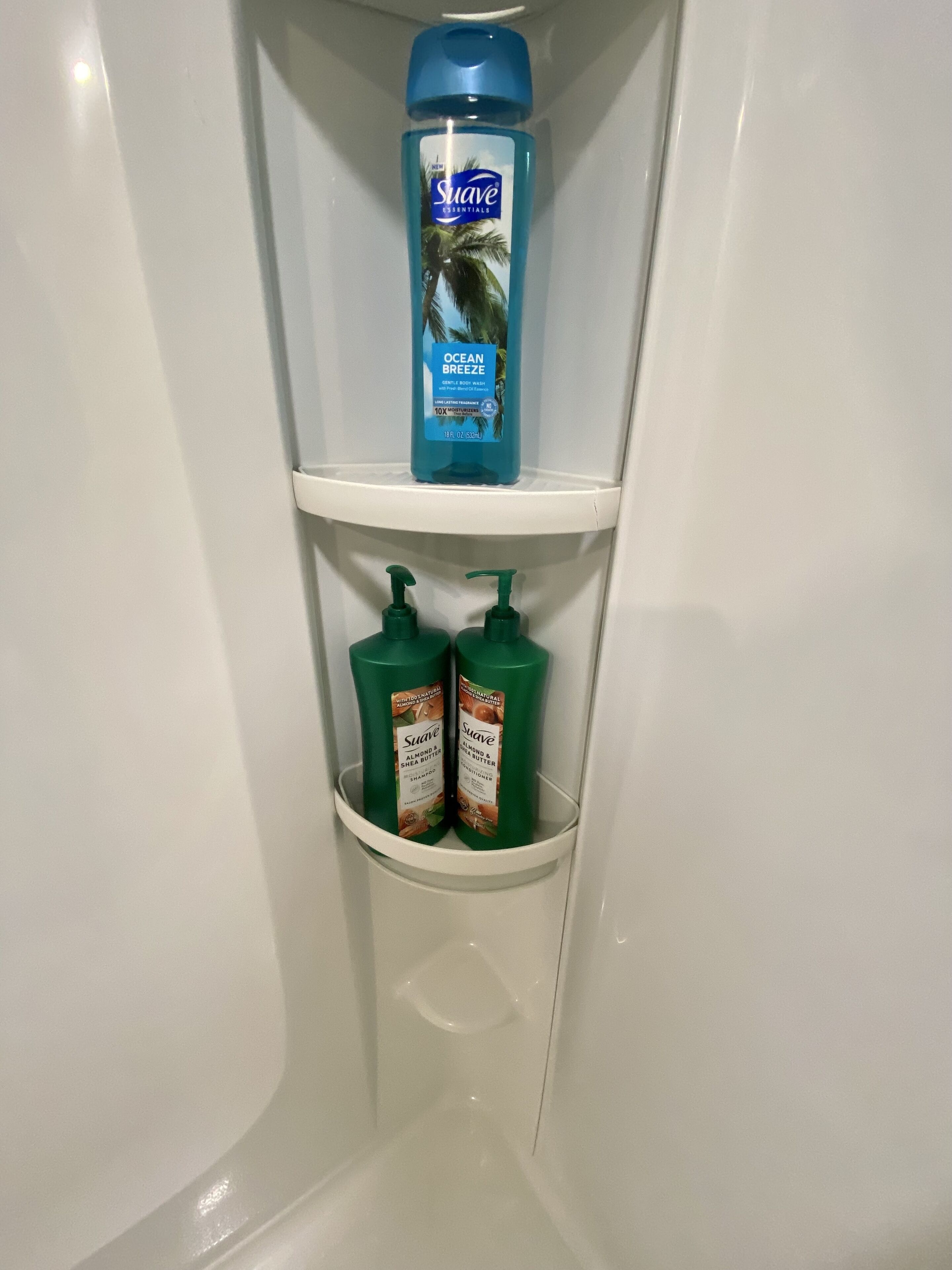 A bathroom shelf with a blue bottle of Suave Ocean Breeze body wash, two green bottles of Suave Almond & Shea Butter shampoo, and a white shelf.