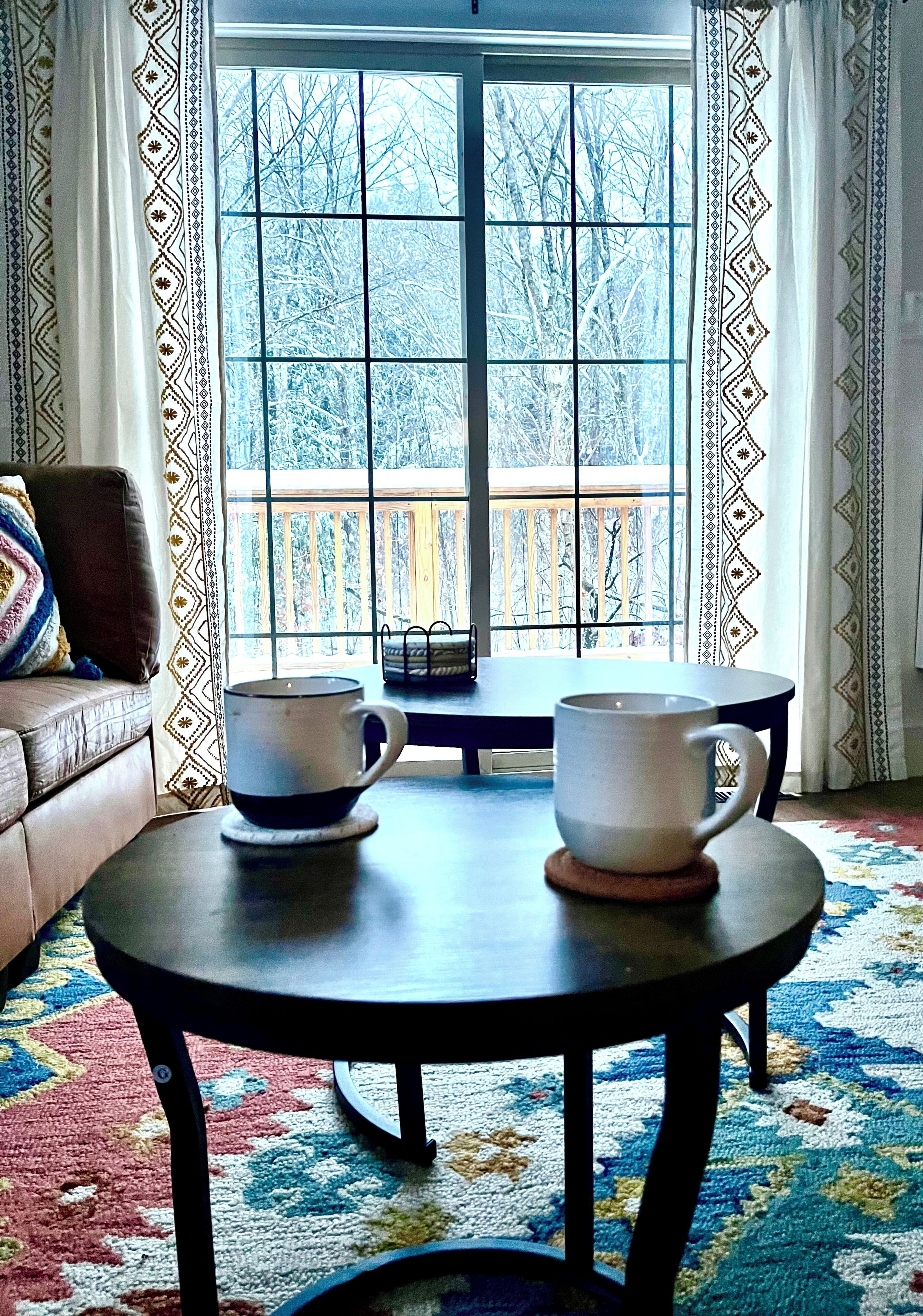 A cozy room with a large window, a sofa, and two tables with cups.