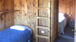 Una habitación tipo cabaña de madera con literas, una escalera y una pequeña mesa con una lámpara.