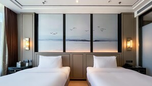 A hotel room with two beds, a large window with a view of the sea and birds, and a wall-mounted artwork. - Grand Madison Jingzhong Yuci Haitangwan (Jinzhong)