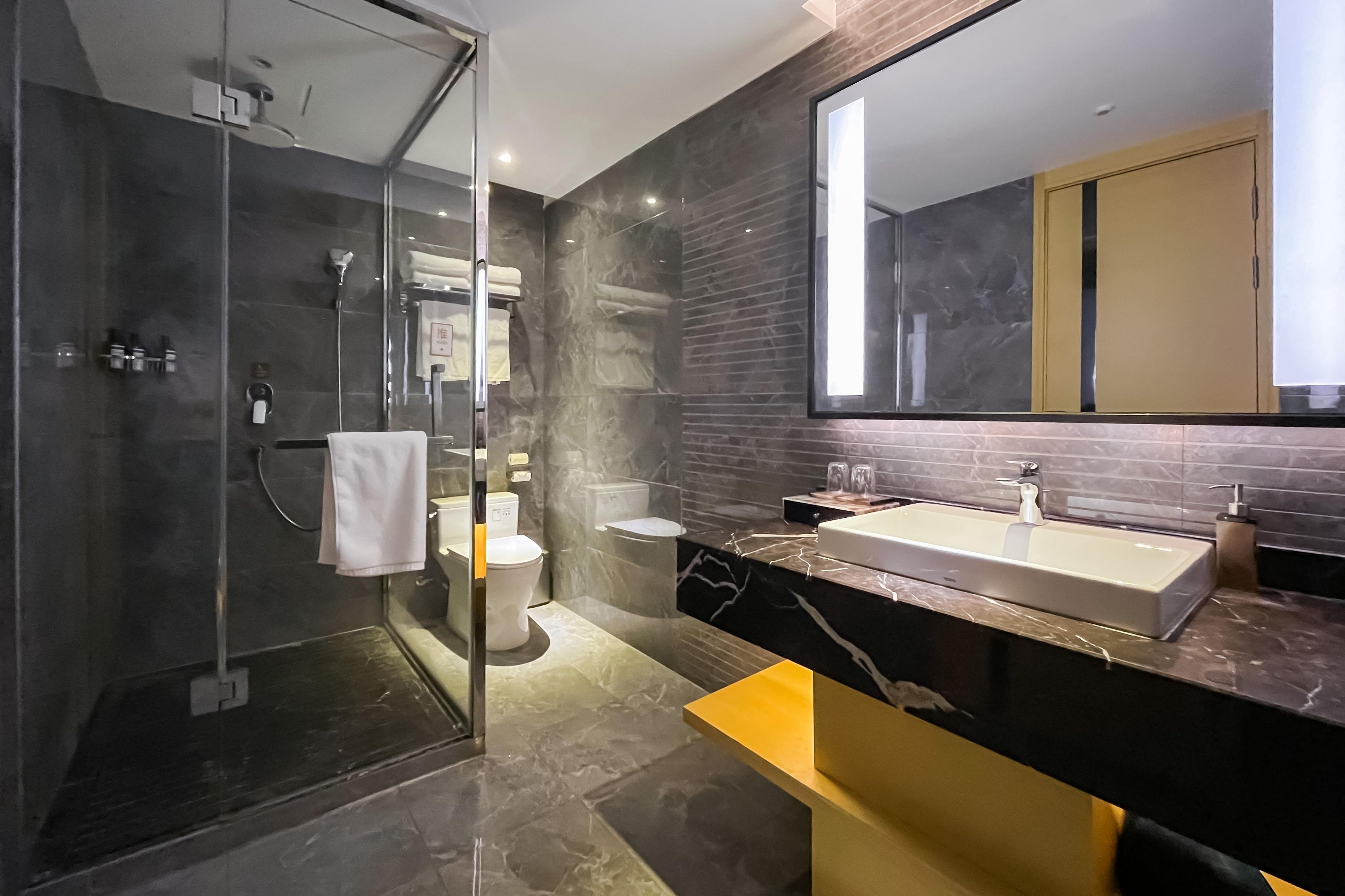 A modern bathroom with a glass shower enclosure, a toilet, and a sink with a marble countertop.