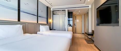 A hotel room with two beds, a TV, a desk, and a view of the sky.