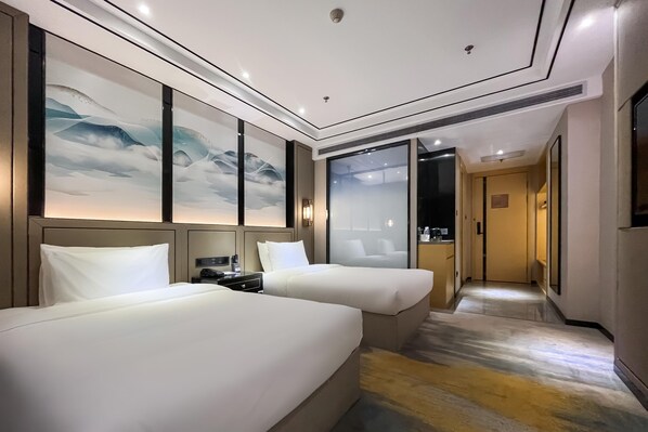 Une chambre d’hôtel avec deux lits, un grand tableau au mur et une vue sur un couloir.
