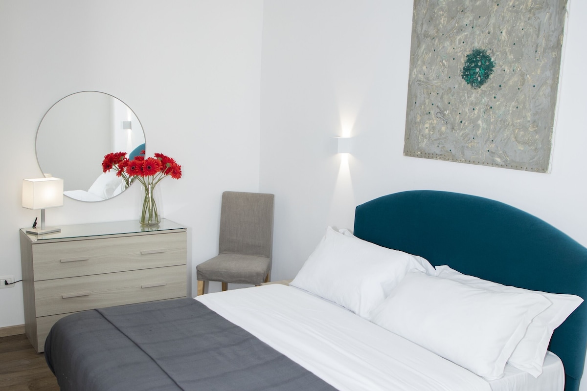 A bedroom with a bed, dresser, chair, and artwork on the wall.