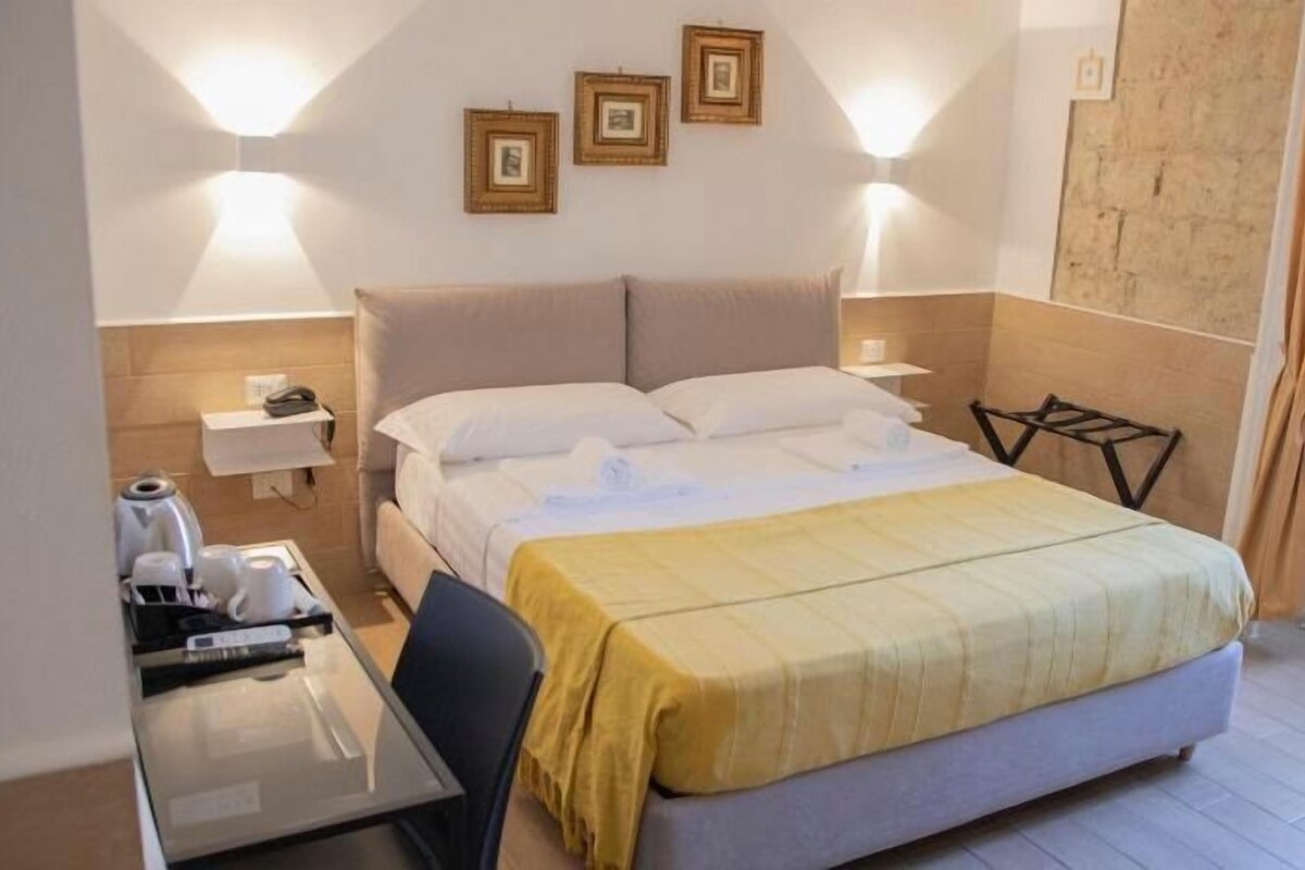 A hotel room with a bed, bedside table, lamp, and a small table with a chair.