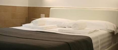 A hotel room with a bed, a headboard, and a wall-mounted light.