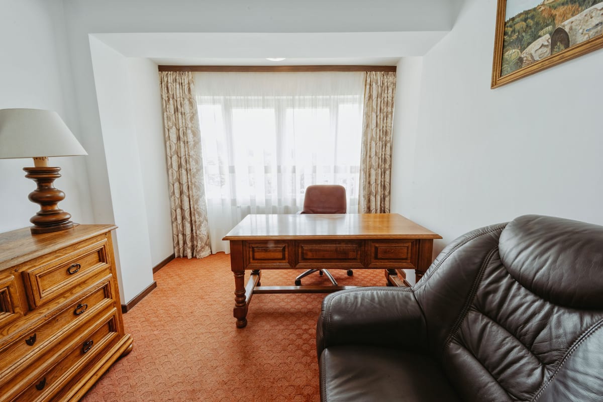 Une pièce comprenant un bureau en bois, un canapé en cuir, une commode en bois et une grande fenêtre avec des rideaux.