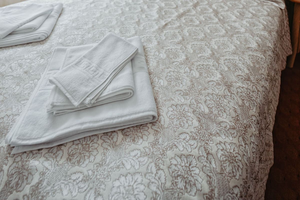 Un lit bien fait, avec une couvre-lit à motifs et des oreillers, une serviette pliée posée sur le lit, une table de chevet avec une lampe et un tableau encadré accroché au mur.