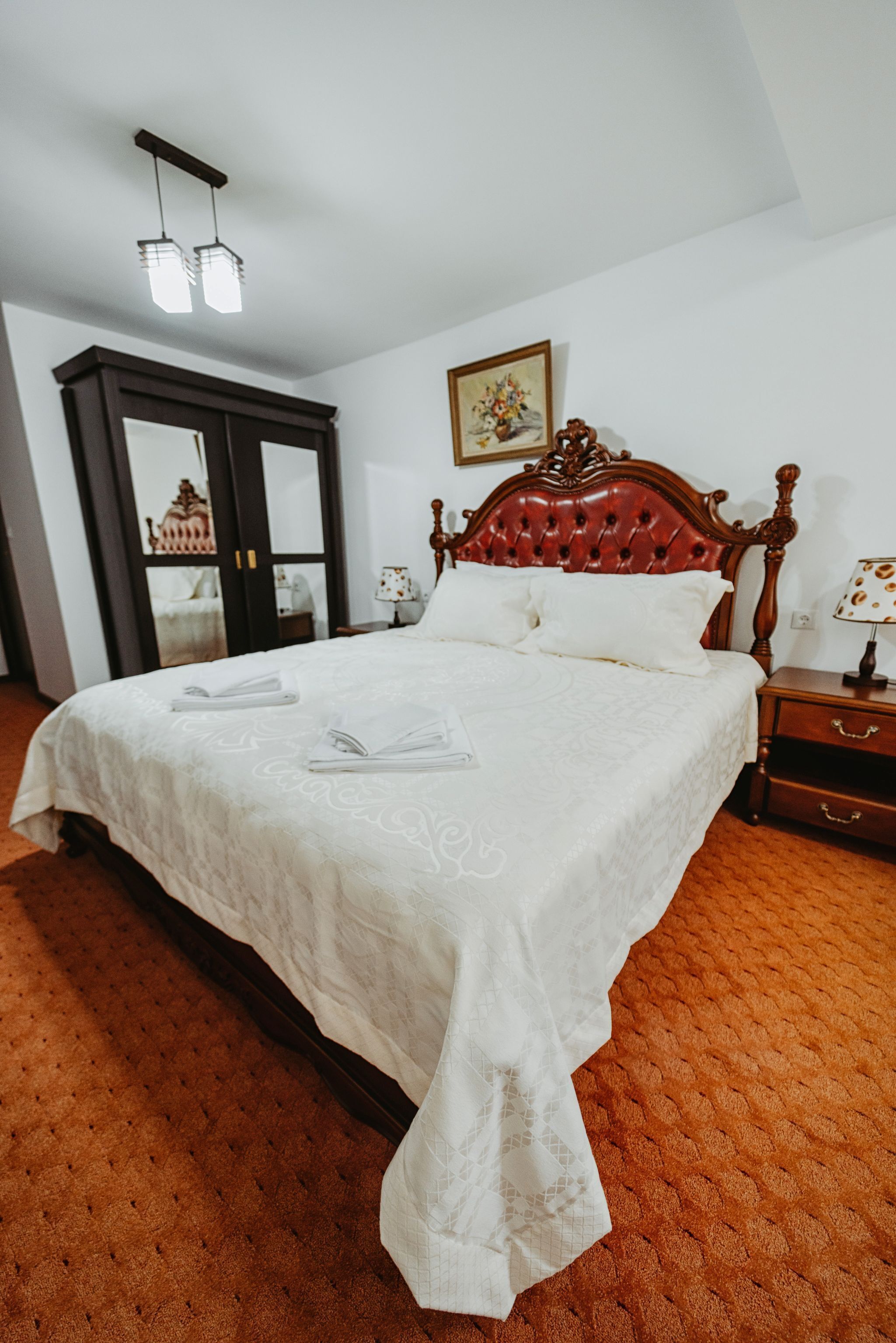 A neatly made bed with a white bedspread, a wooden headboard, and a nightstand with a lamp.