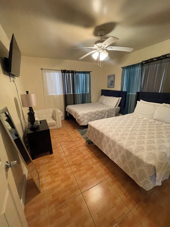 Une chambre d’hôtel avec deux lits, un ventilateur de plafond, une télévision, une lampe et une fenêtre avec des rideaux.