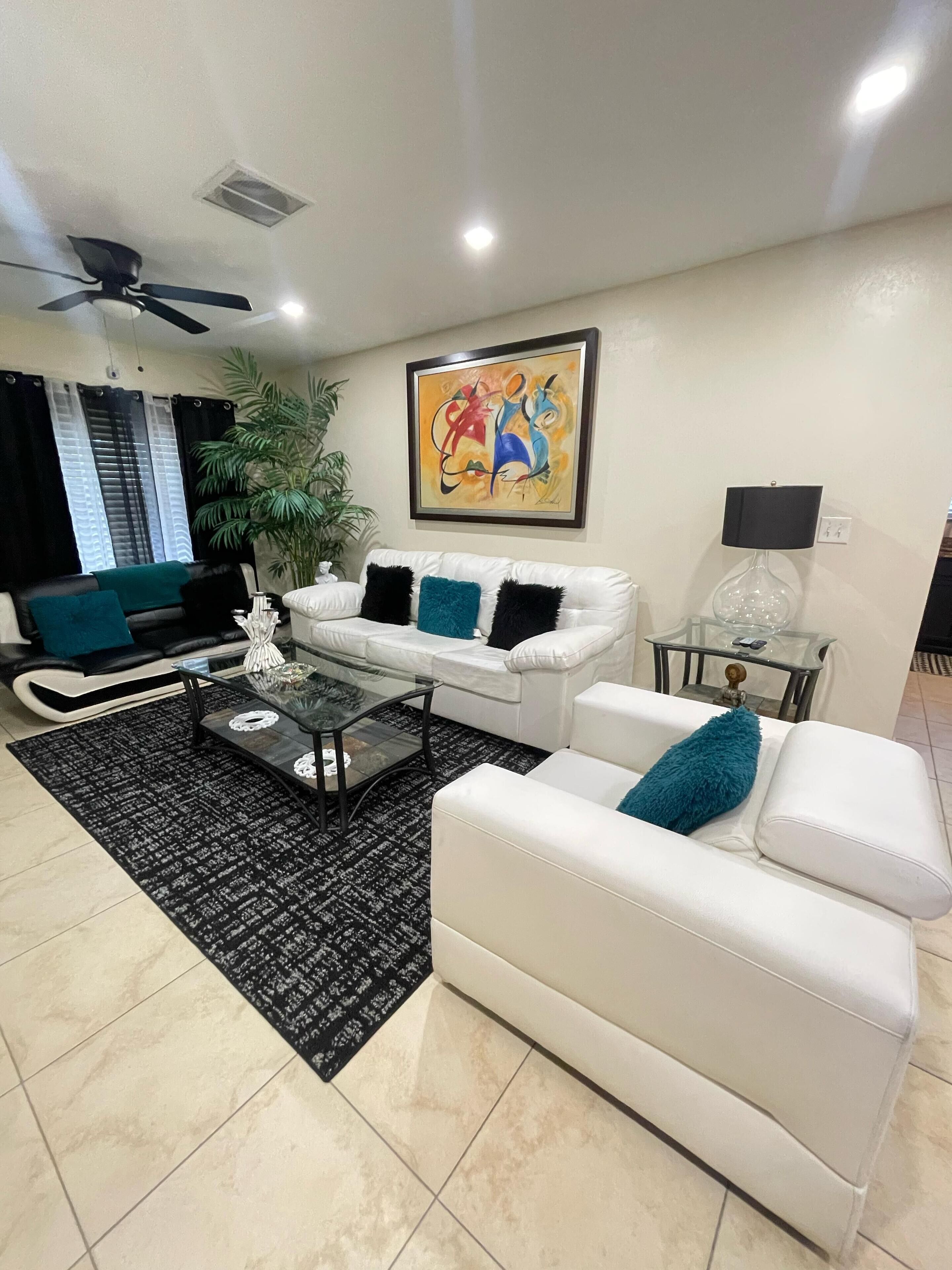 A modern living room with a white sofa, a glass coffee table, and a ceiling fan.