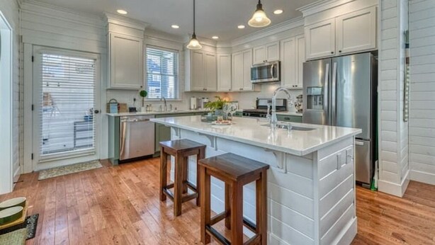 A modern kitchen with white cabinets, stainless steel appliances, and wooden stools. - Oceanside - Dog Friendly - 3pm Checkout   (Pacific Beach)