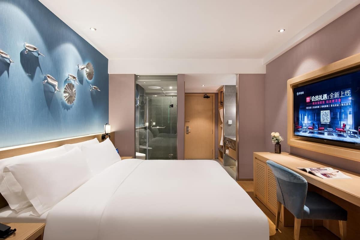 Een hotelkamer met een groot bed, een bureau met een stoel, een televisie en een douchecabine met glazen wanden.