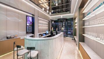 Un moderno vestíbulo de hotel con un mostrador de recepción curvo, taburetes de bar y una vitrina con objetos.