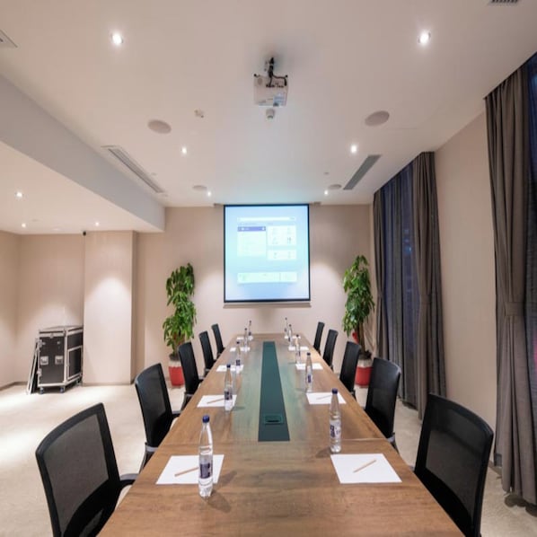 A conference room with a long table, chairs, a projector screen, and potted plants.
