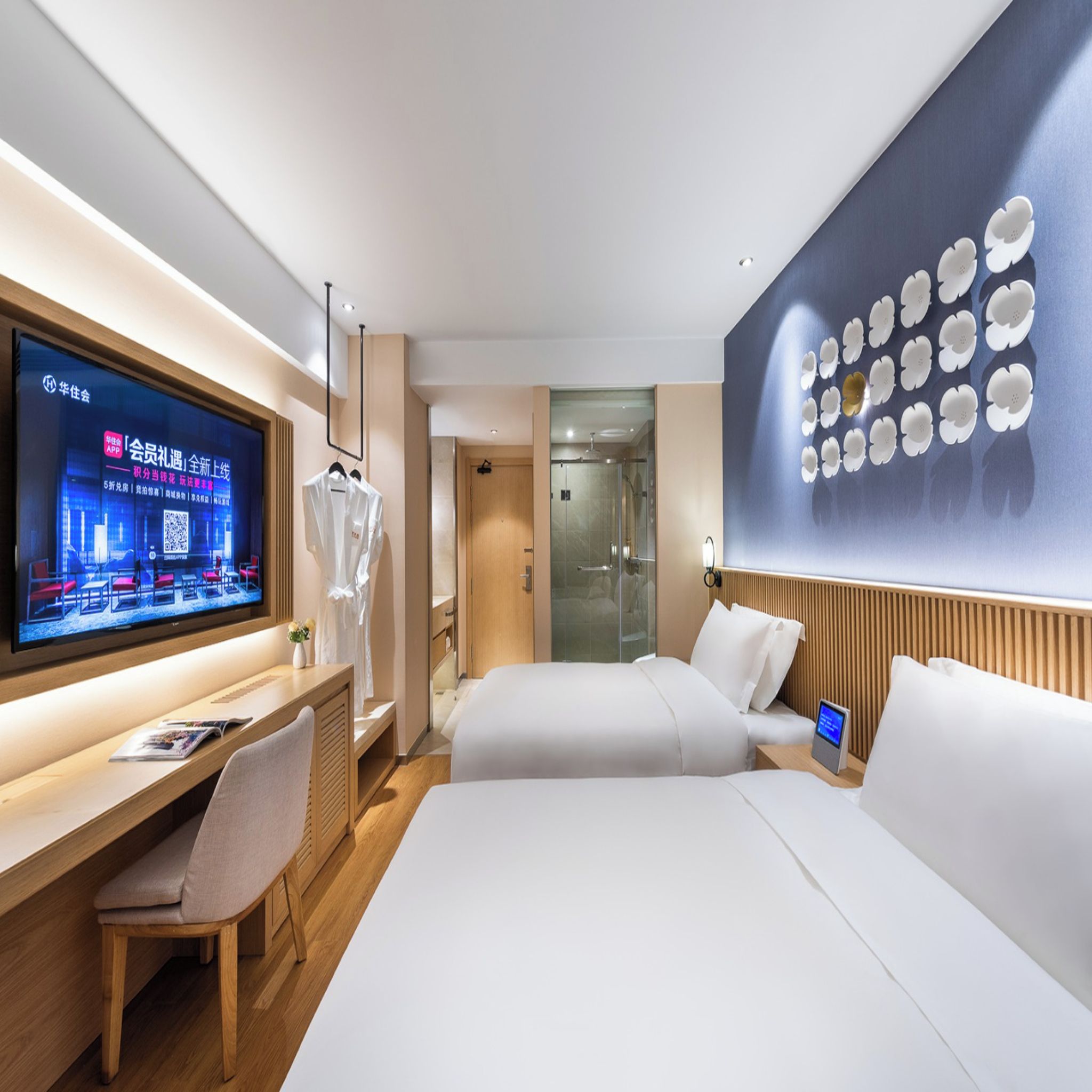 Una habitación de hotel moderna con una cama, mesita de noche, televisor y una pared decorada con motivos florales.